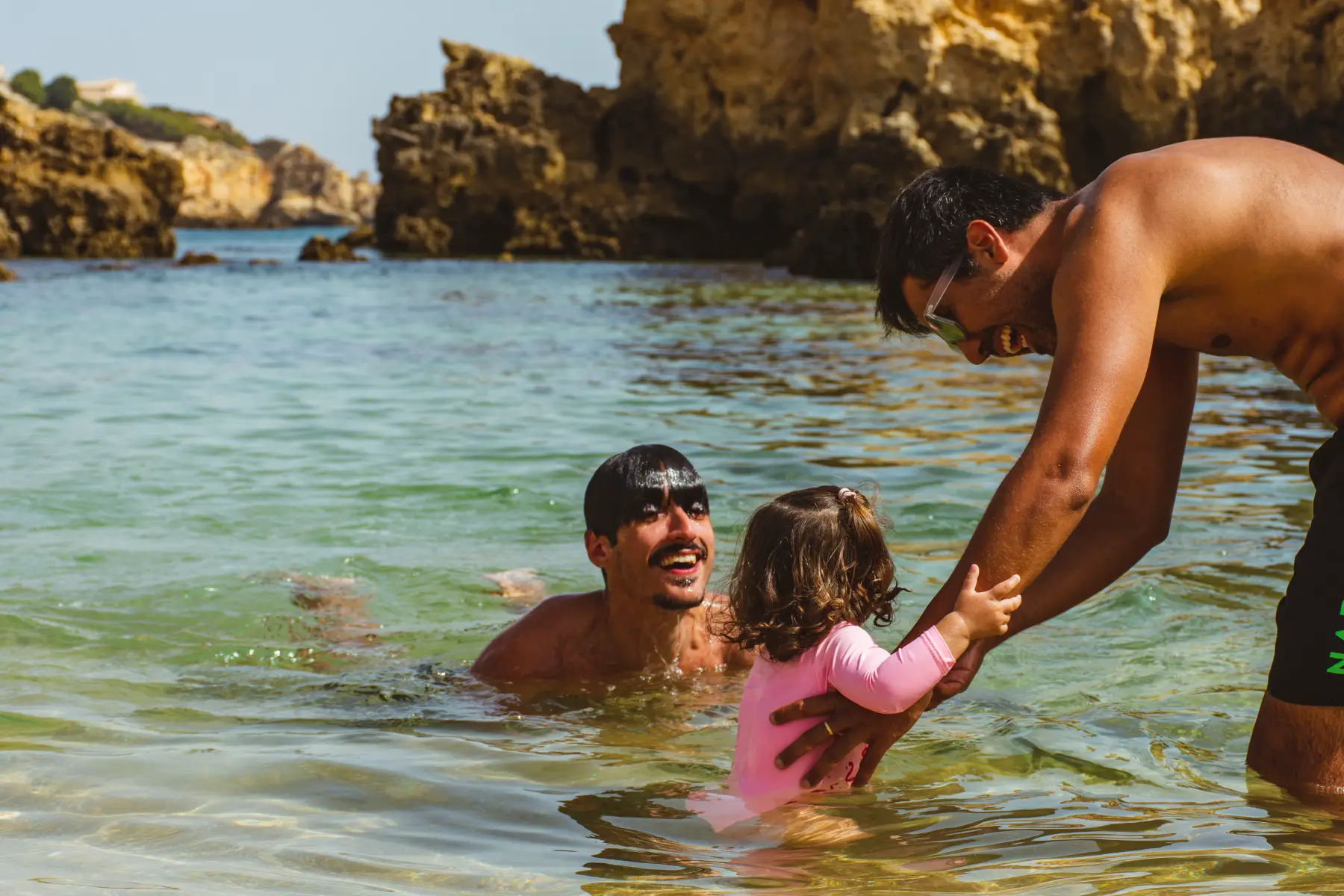 two men playing and swimming with a little girl at Arrifes beach in Albufeira, Algarve