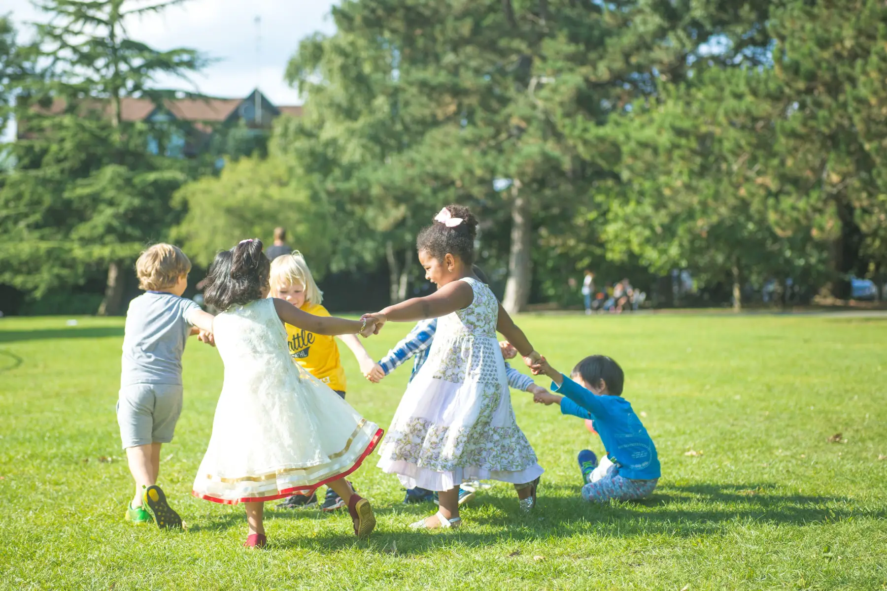 A group of young children holding hands and playing in a circle in a park on a sunny day