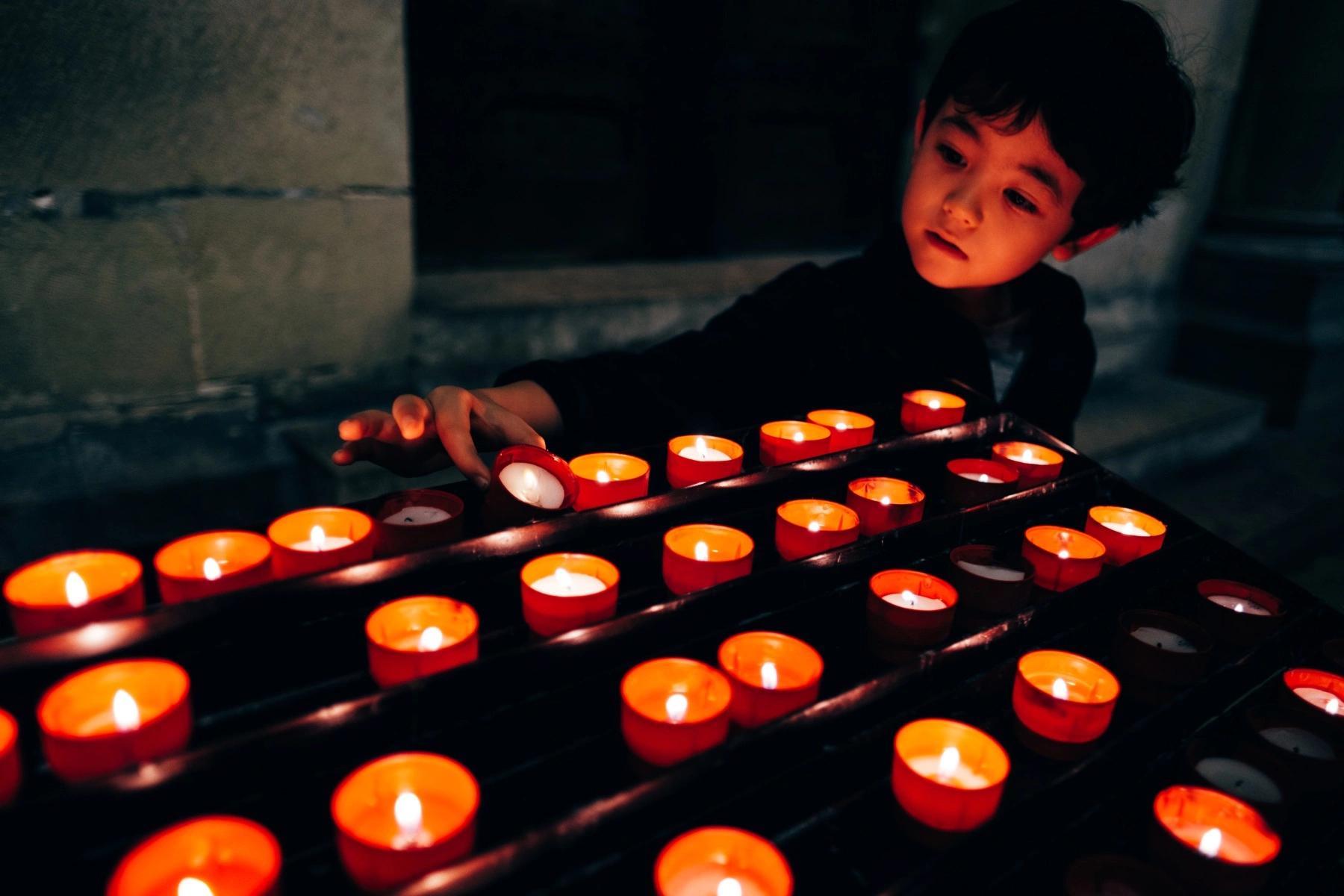 a young boy placing a Votive candle (prayer candle) among others inside a church in Lisbon