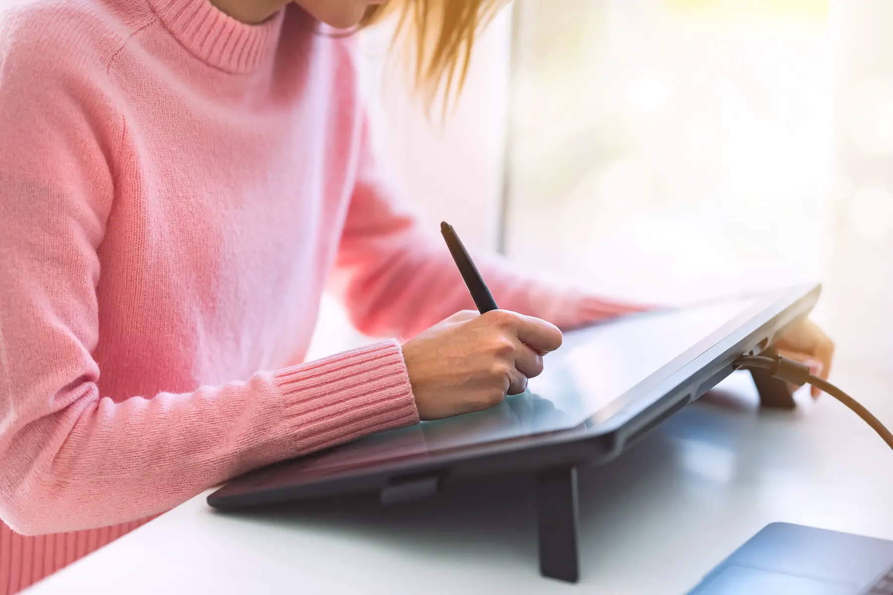 Close-up of a person in a pink jumper using a graphic design tablet