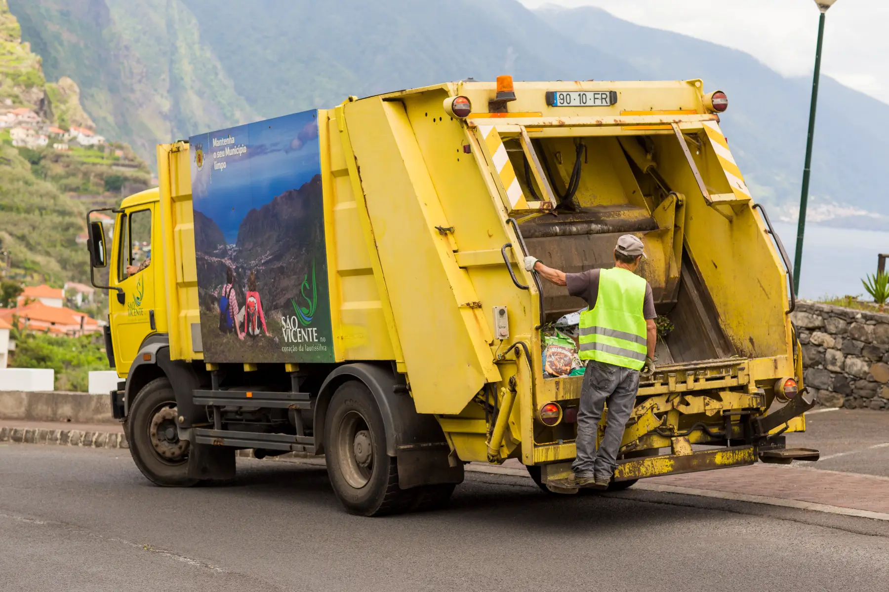 A yellow garbage truck driving through the hills of Portugal