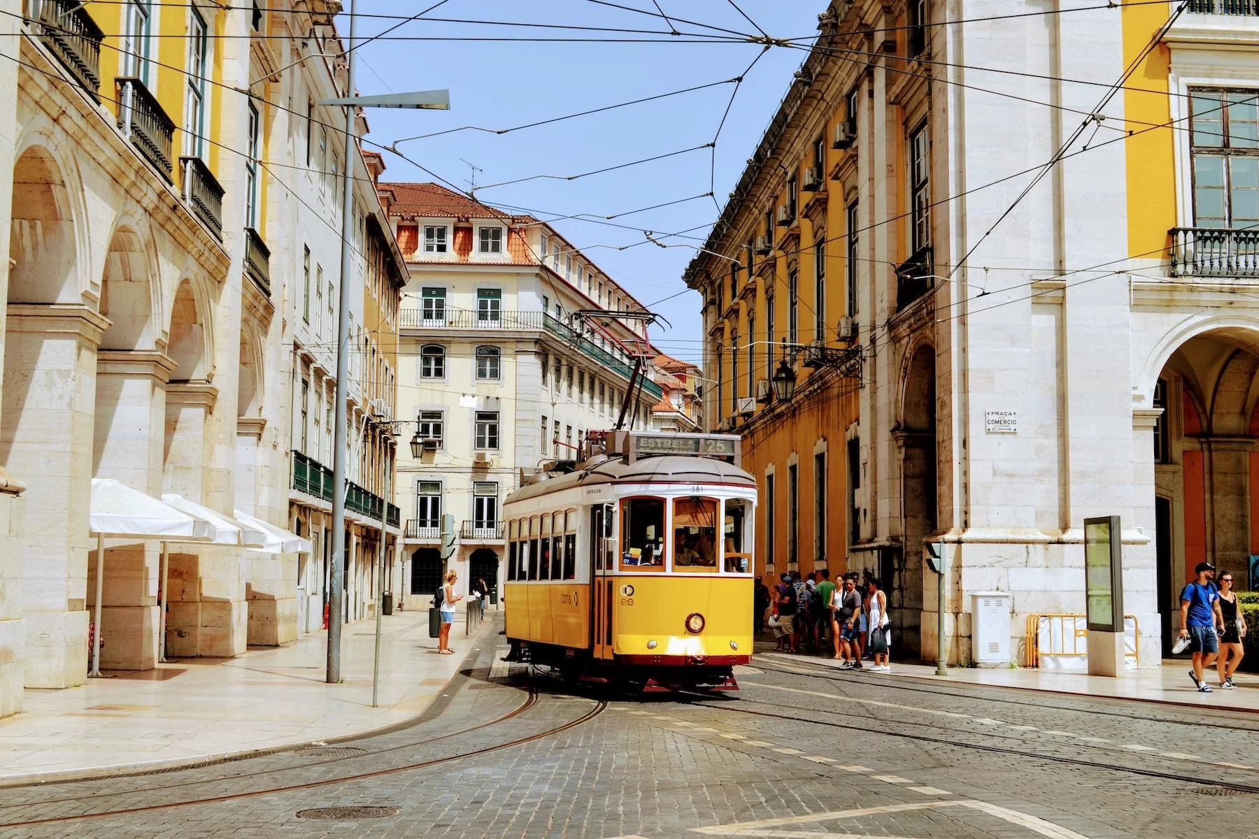 a yellow tram drives down the streets of Lisbon on a sunny day
