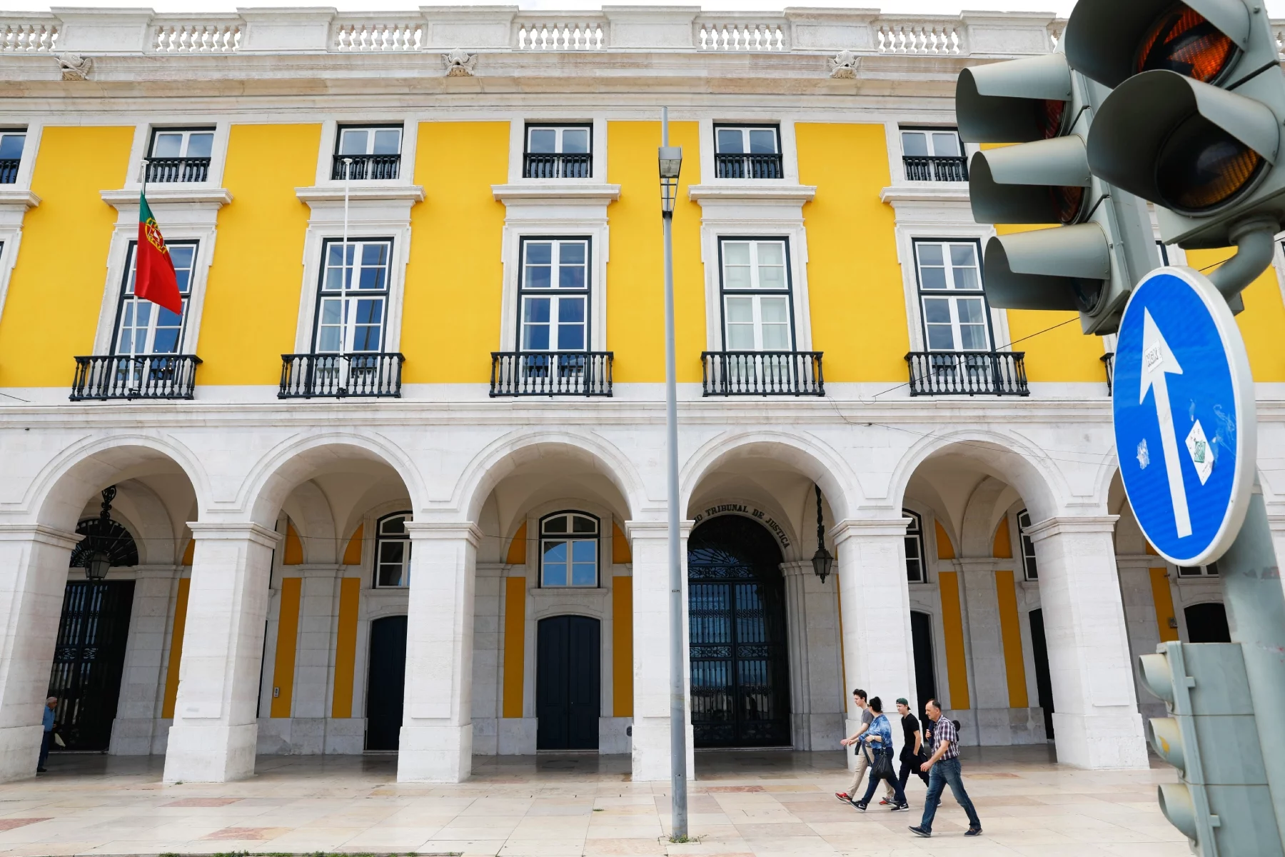 People walking pas the Ministry of Justice in Portugal: large, grand, old-fashioned building, yellow edifice.