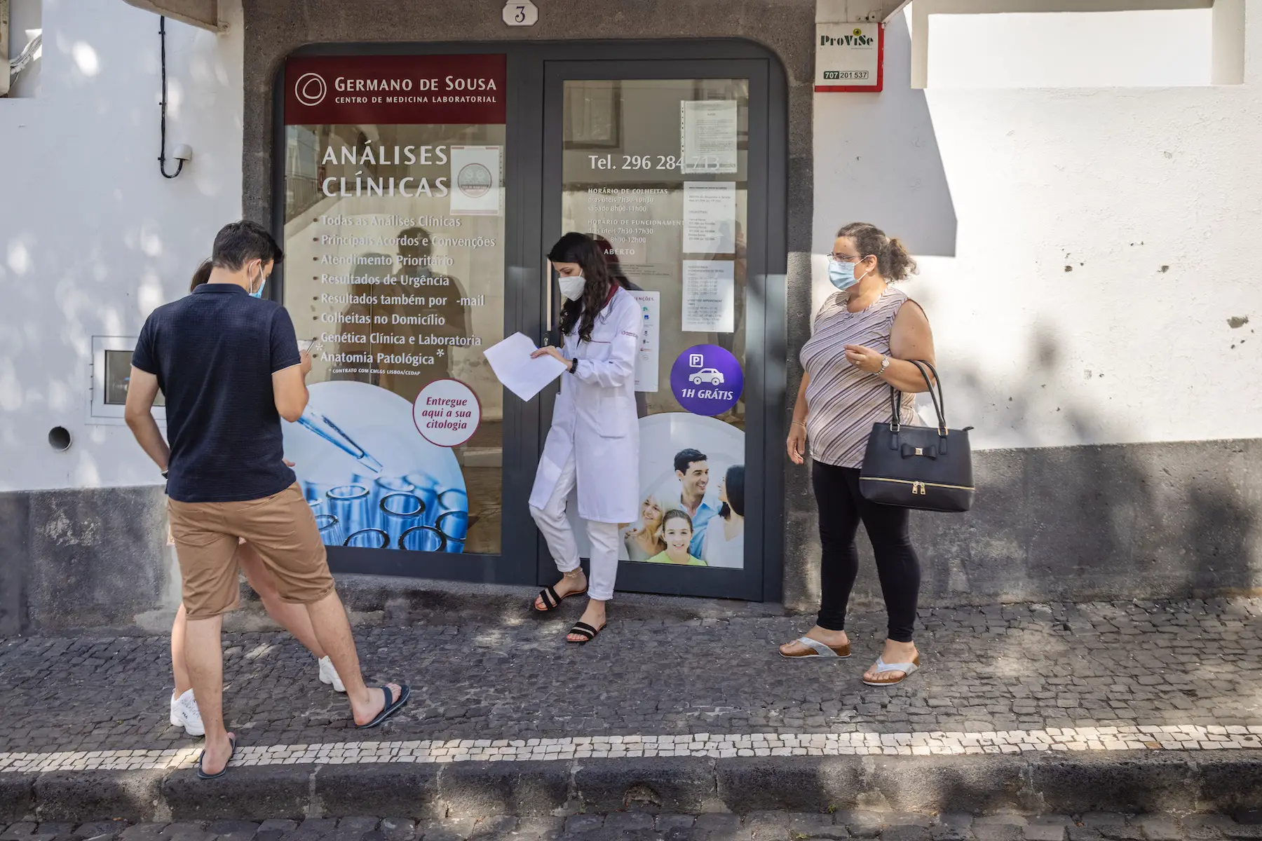 People stand on the sidewalk outside a medical clinic during the COVID-19 pandemic in the center of Ponta Delgada, Portugal
