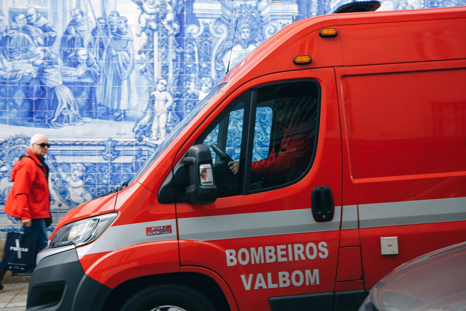 A bright red ambulance is parked on a street in Lisbon right in front of a wall decorated with azulejo tiles