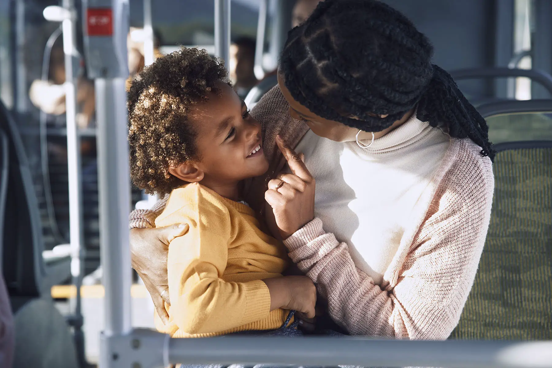 Mother looking at her smiling child, while holding them in a close hug on public bus.