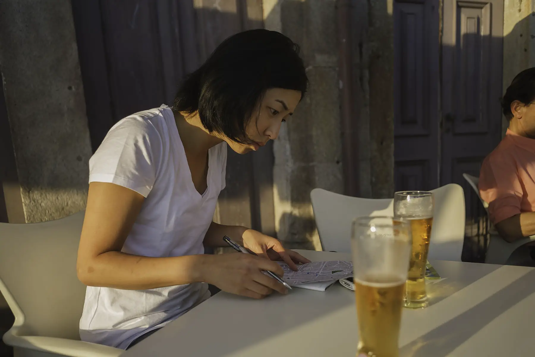Young non-binary sitting at a cafe looking at a map while drinking beer.