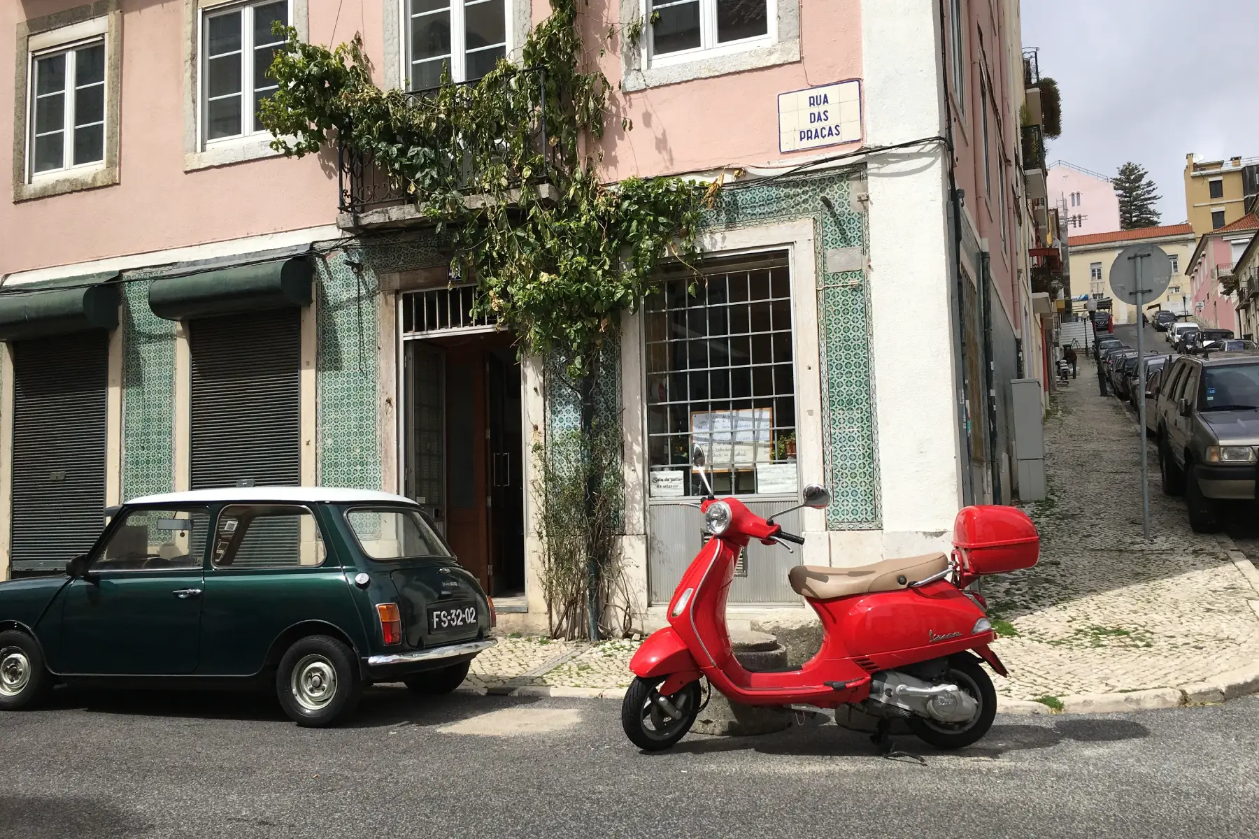 a red moped parked next to a car on a quiet street in Lisbon, Portugal