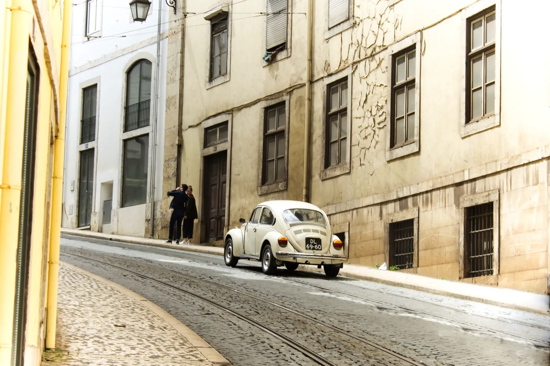 a white Beetle driving along an old cobbled street in Lisbon