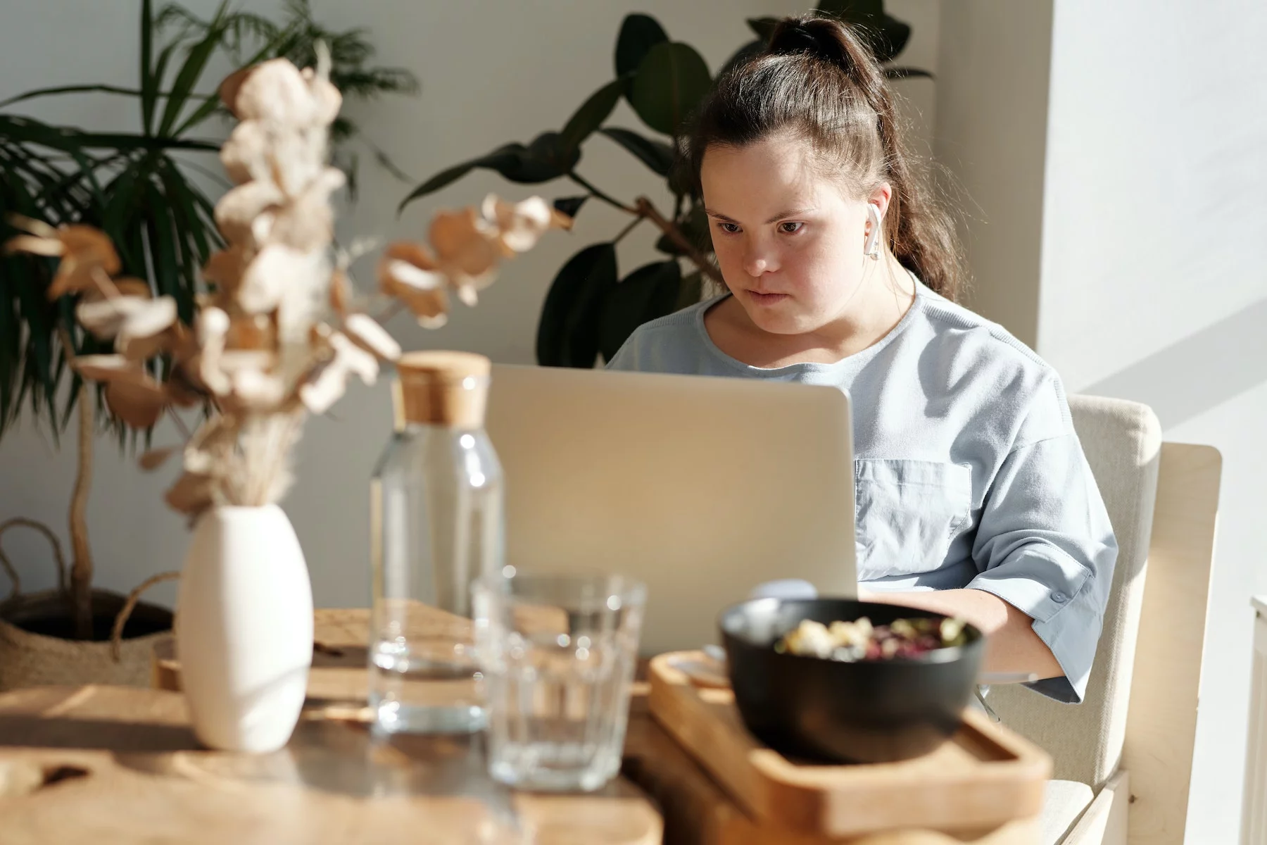 a woman sits working on her laptop at a cafe with plants in the background