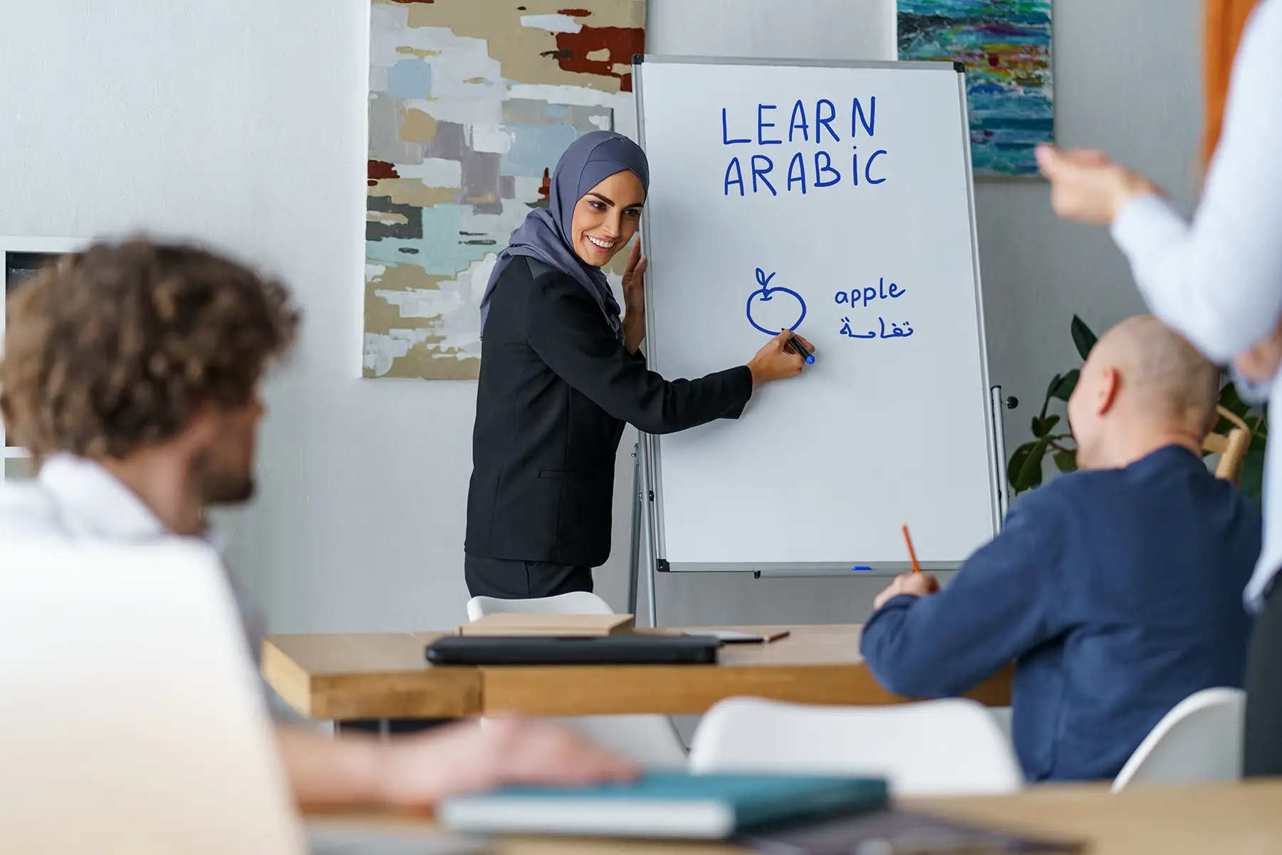 Arabic lesson: teacher has drawn an apple and written 'apple' in English and Arabic on the board