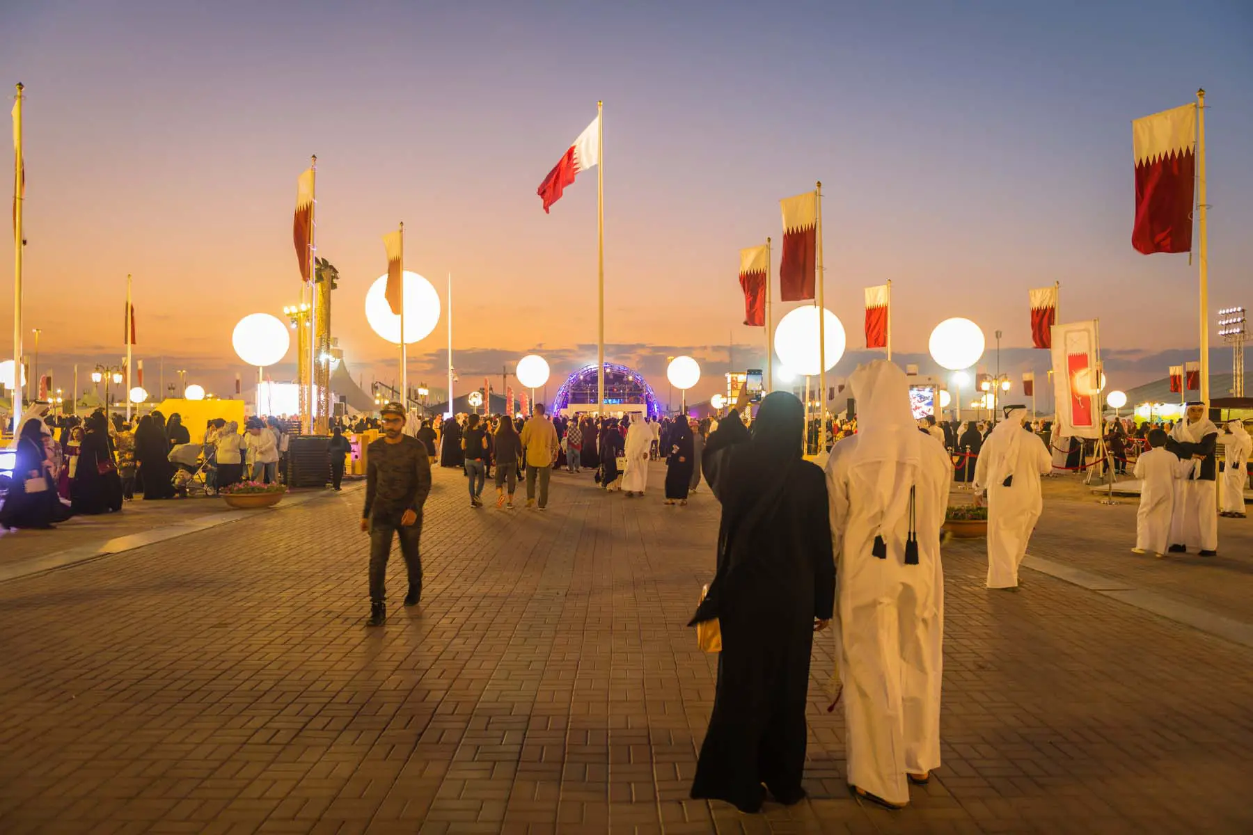 crowds walk through Doha at dusk, the pavement lit with lights.