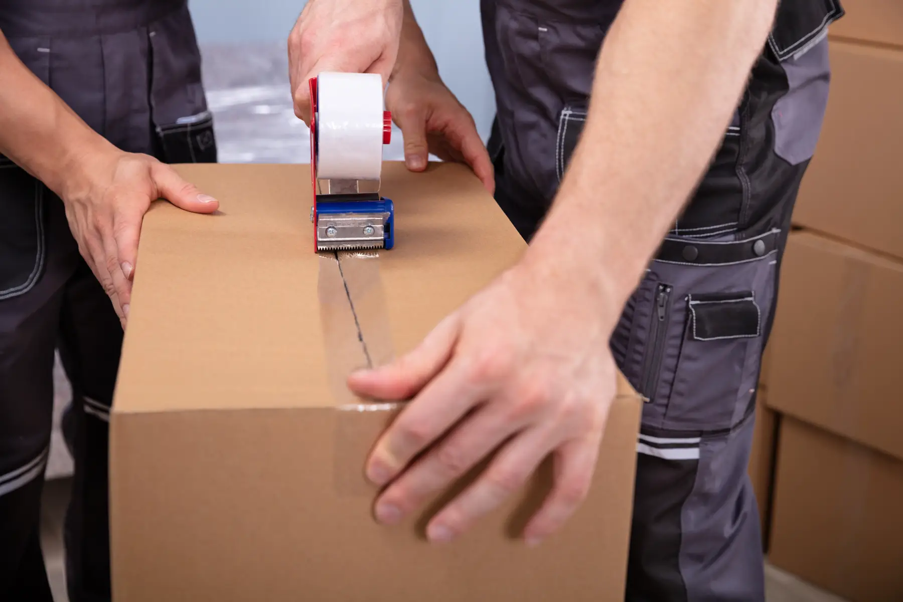 professional movers packaging cardboard boxes with a tape gun