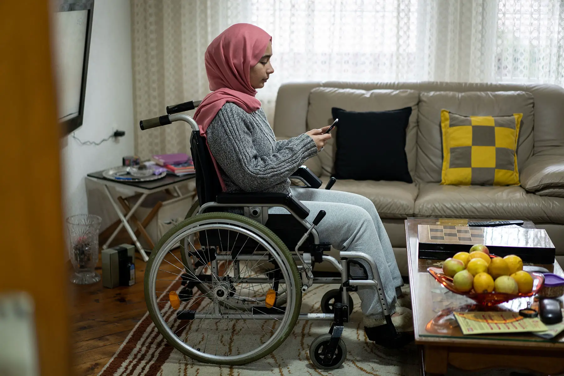 Woman in a wheelchair at home, looking at her cell phone.
