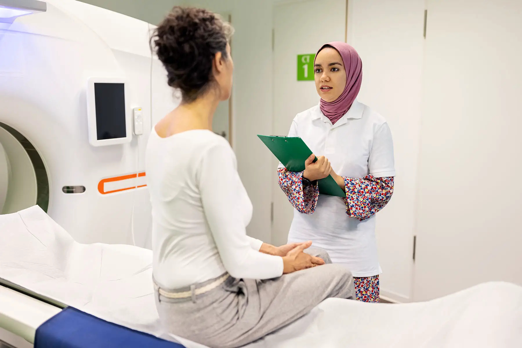 Doctor asking information to female patient before CAT scan test in examination room.