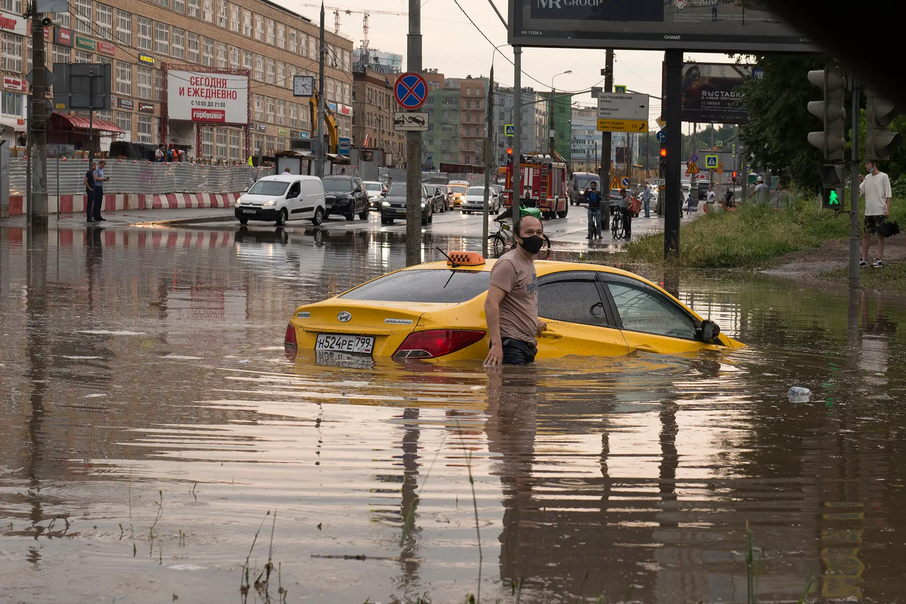 A man in Moscow stands in floodwater next to his car