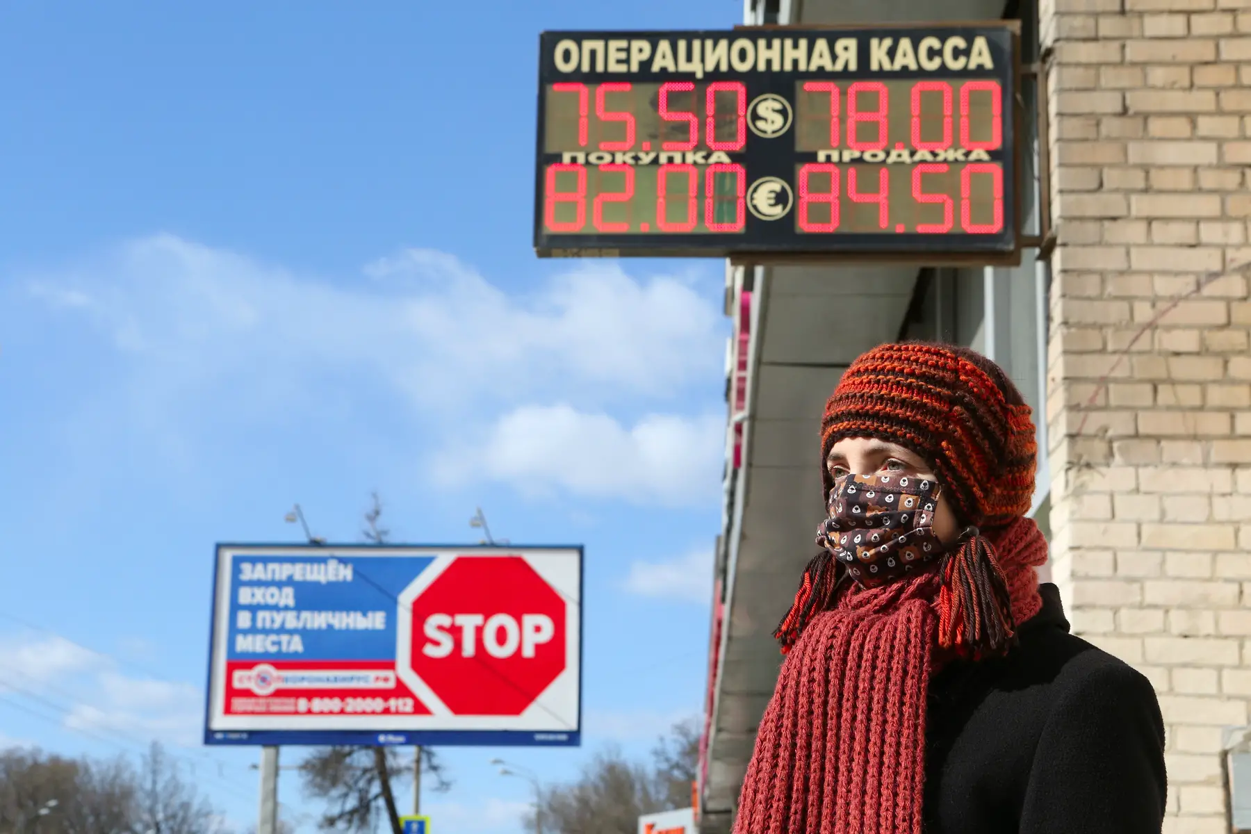 Masked woman stands near electronic exchange rate board during COVID-19 in Russia