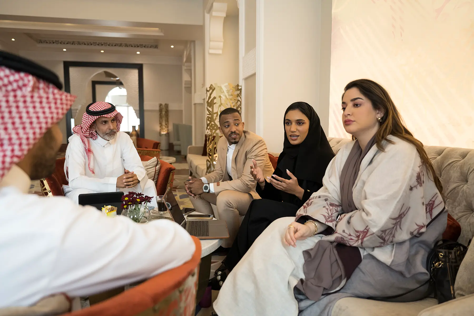 Entrepreneurs in traditional Saudi dress and suits conduct a business meeting in the lobby of a hotel