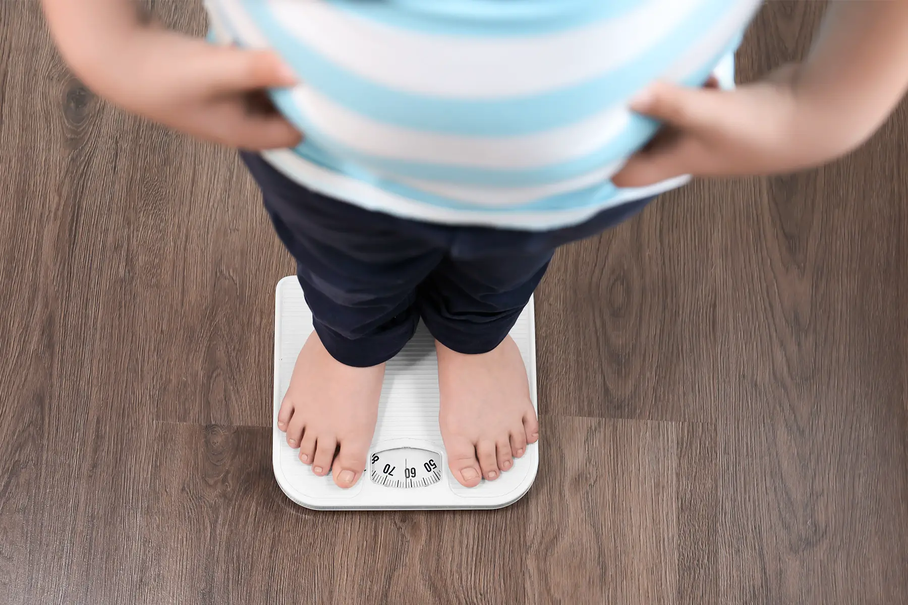 an overweight boy standing on floor scales indoors