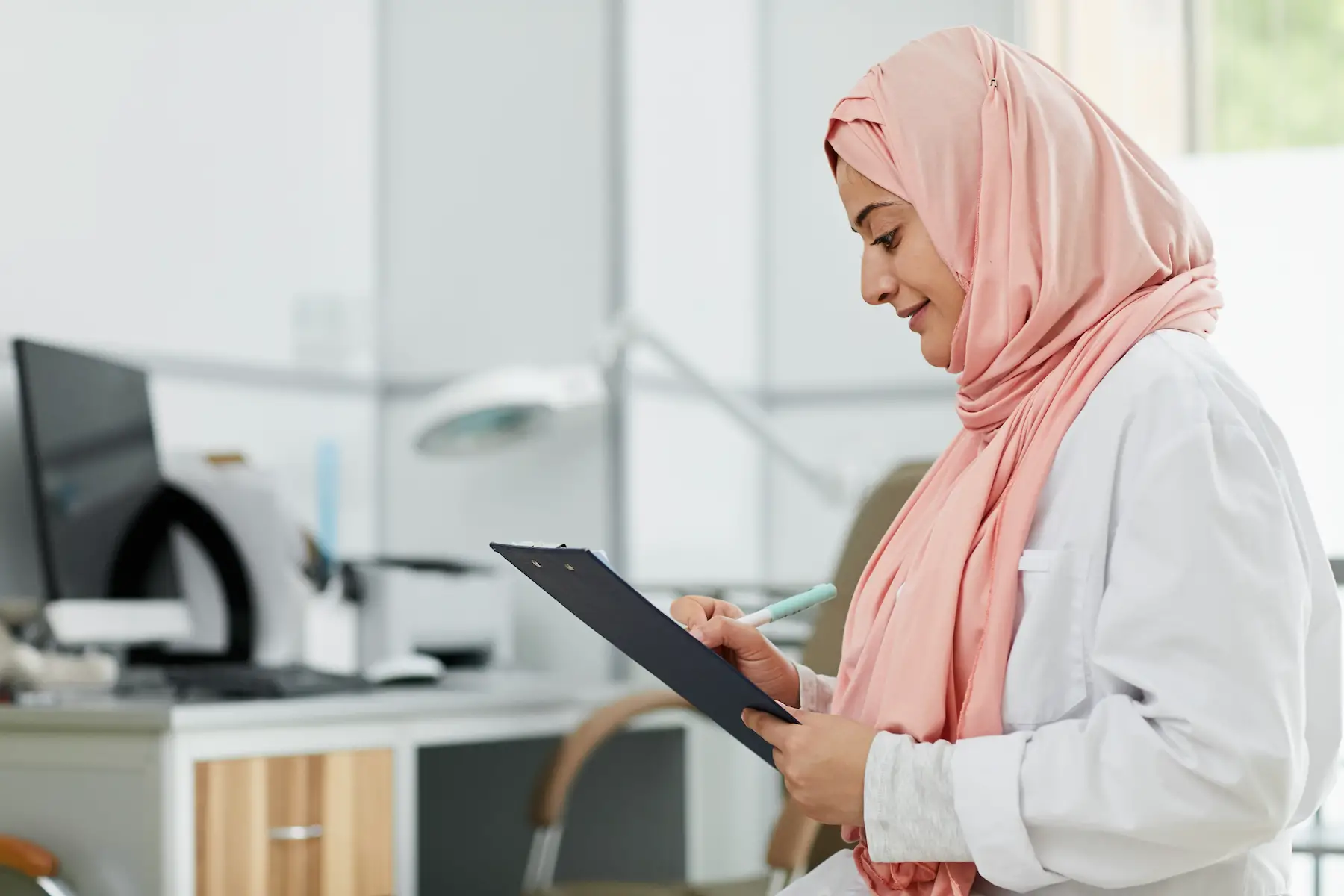 Female Muslim doctor wearing a hijab looking at a patient's chart.