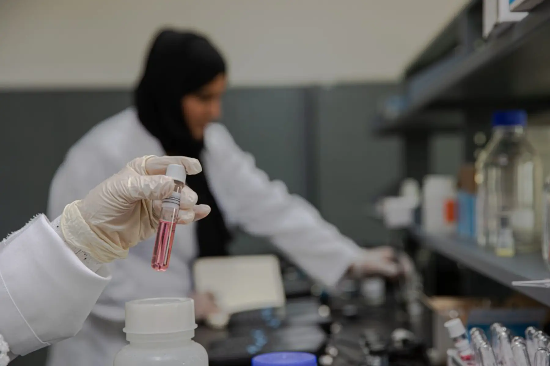 testing samples in lab - technician with hijab in background