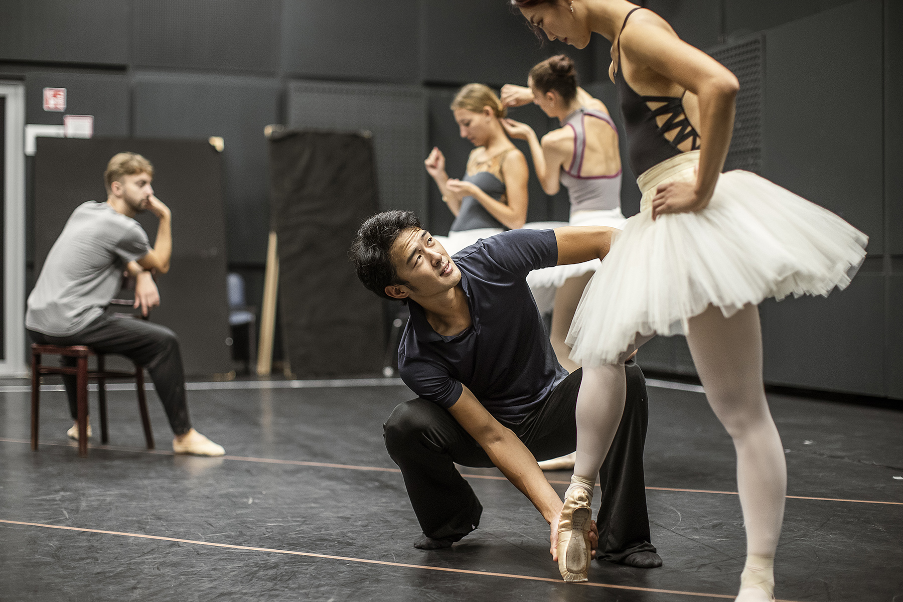 A choreographer manipulates a ballet dancer's pointed foot, standing on a black stage as they rehearse for a show on stage, with their special arts talent, they can apply for a work visa in Singapore