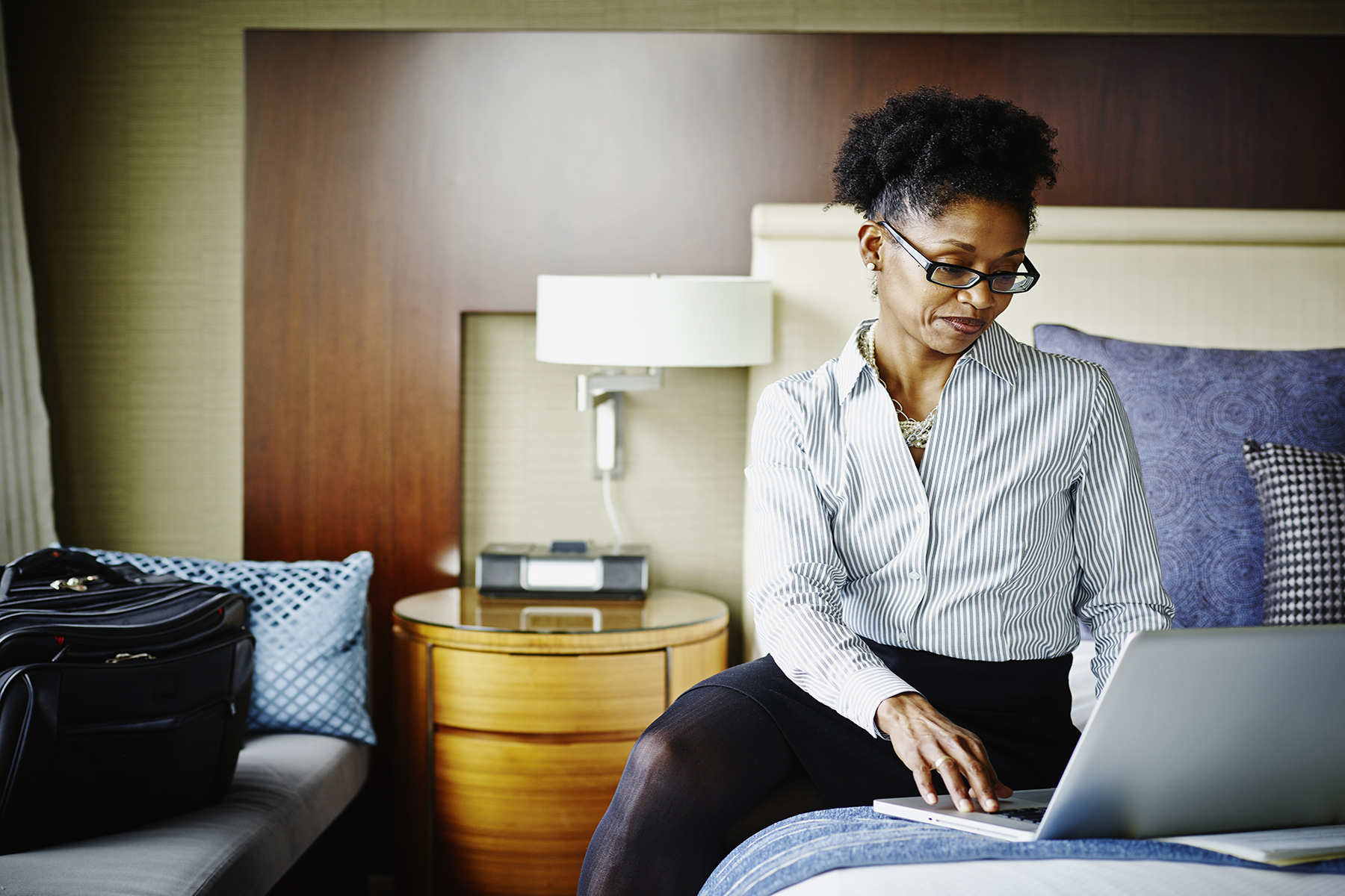 Business woman sits on her bed in her hotel room and works on her laptop