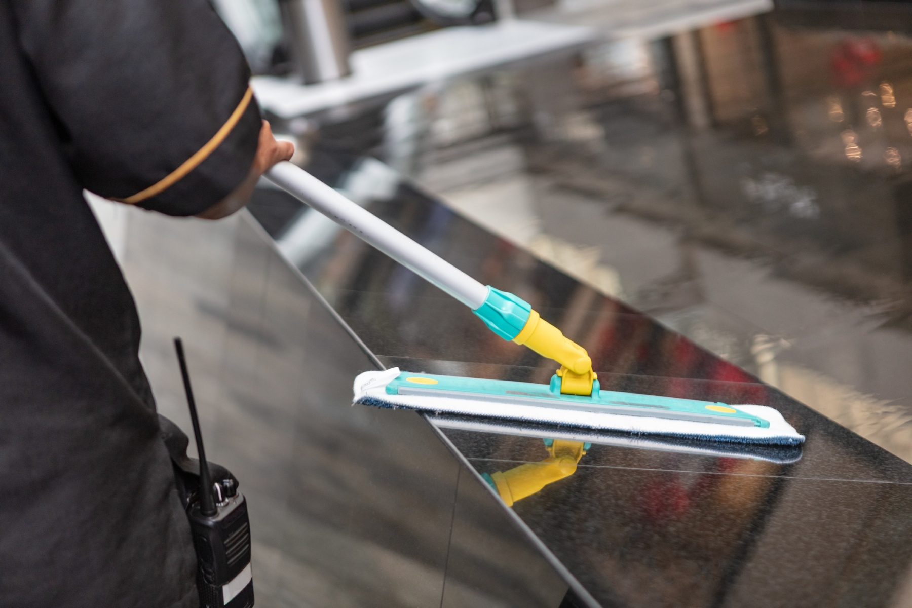 a close-up of a cleaner holding a mop and cleaning the side panel of an escalator