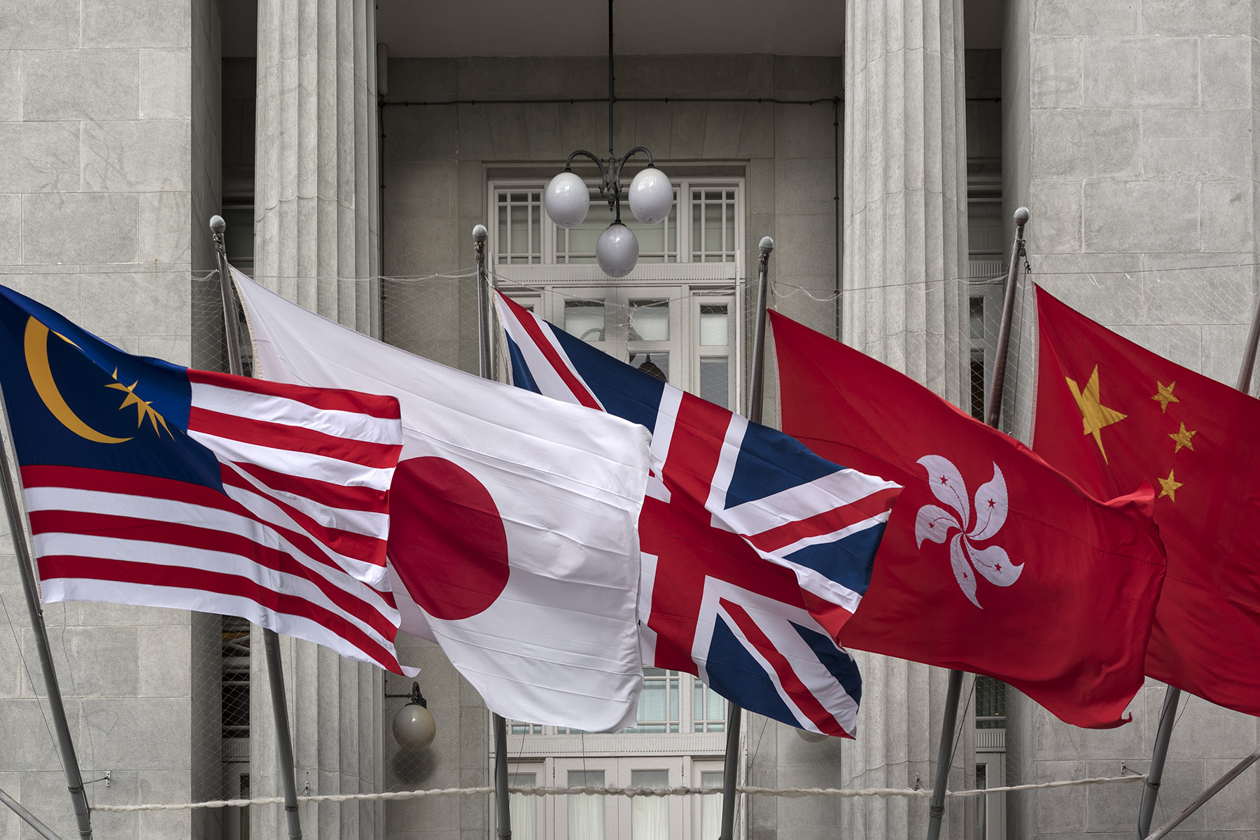 Row of flag poles outside a building with the flags of Malaysia, Japan, United Kingdom, Hong Kong and China