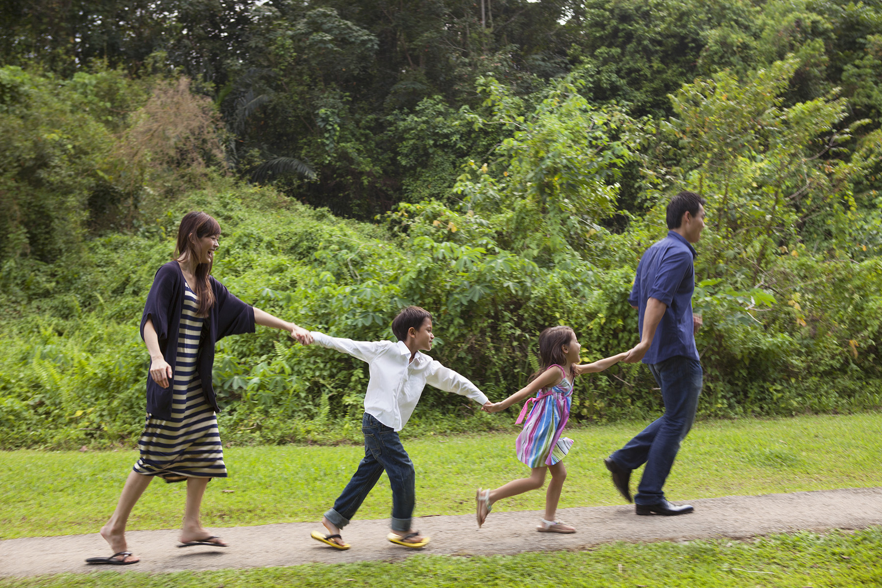 Family walks along path in a park holding hands and laughs

