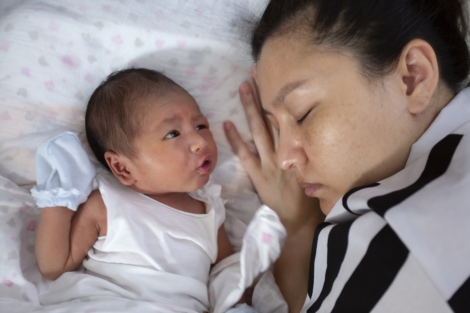 Tired mother sleeps next to awake newborn, she could hire a nanny but would need a work visa for Singapore