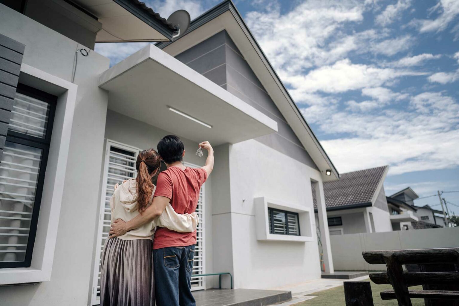 Couple embracing while looking at their new home. The man is holding up the keys in the air.