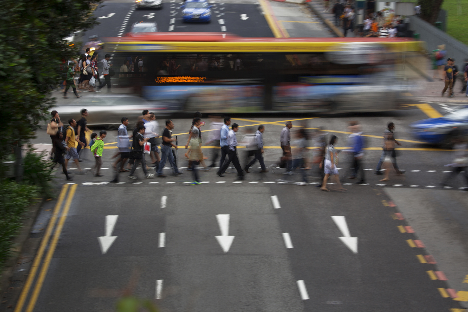 Movement blur of bus in background as people cross a busy street in Singapore