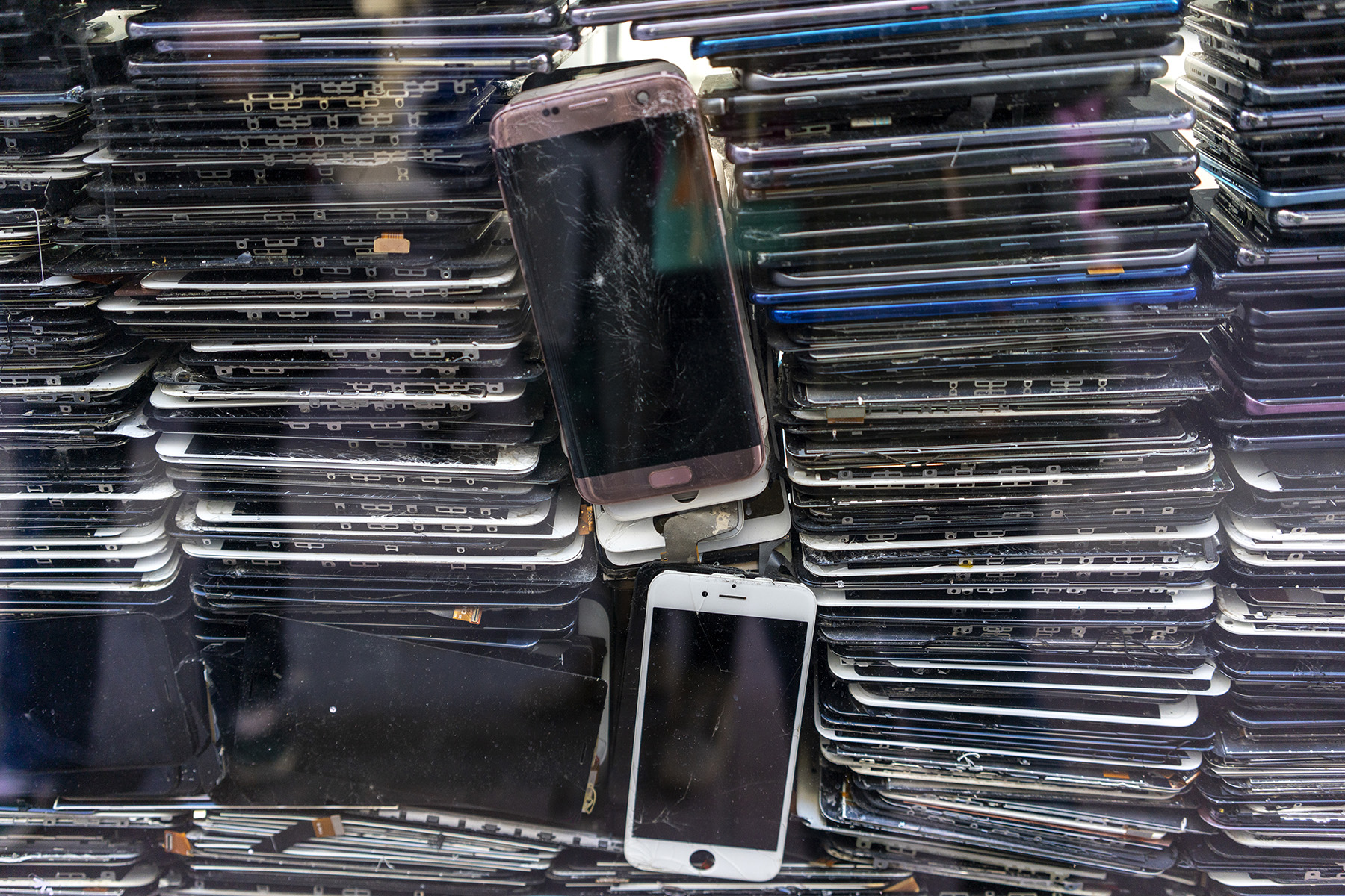 Piles of discarded mobile phones and tablets behind a window