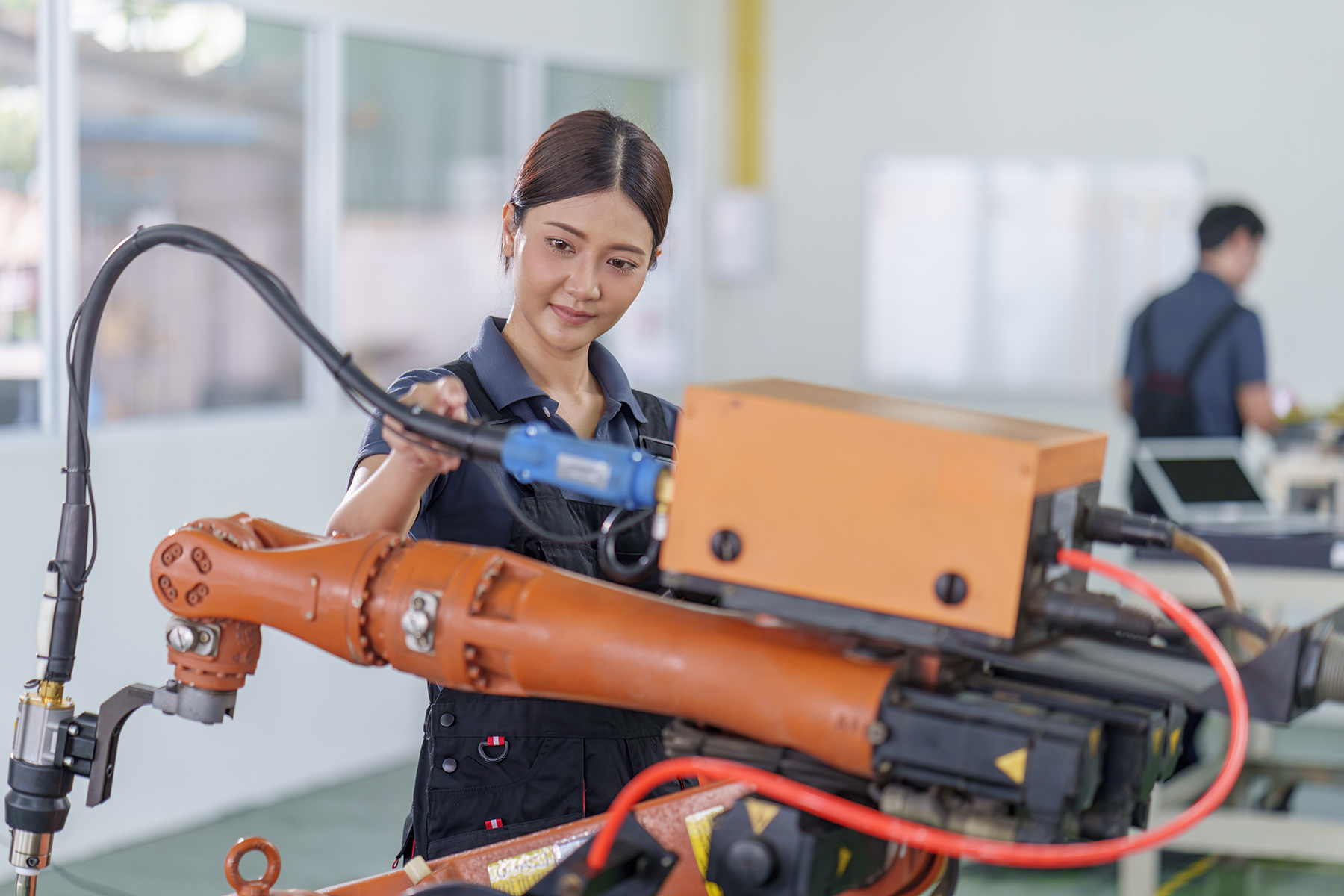 An engineer trainee/student works or trains on an orange robotics machine to gain practical skills
