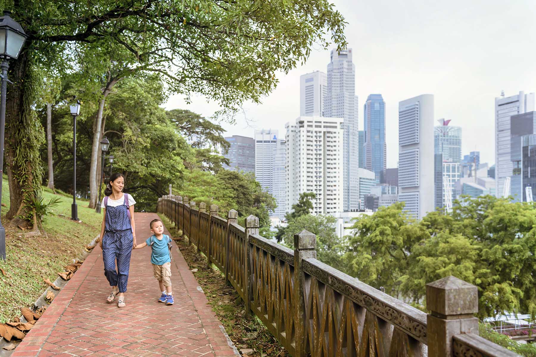 Mother and son are walking through a park, Singapore city is visible in the background.