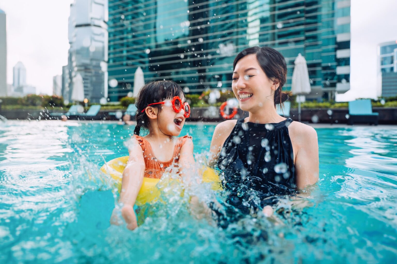 Mother and daughter laugh and splash around in a pool together outside