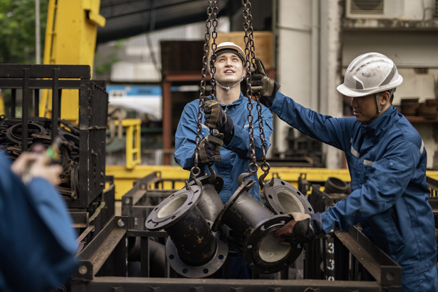 Engineers or technicians wearing hard hats and blue overalls lowers down parts of a machine with chains