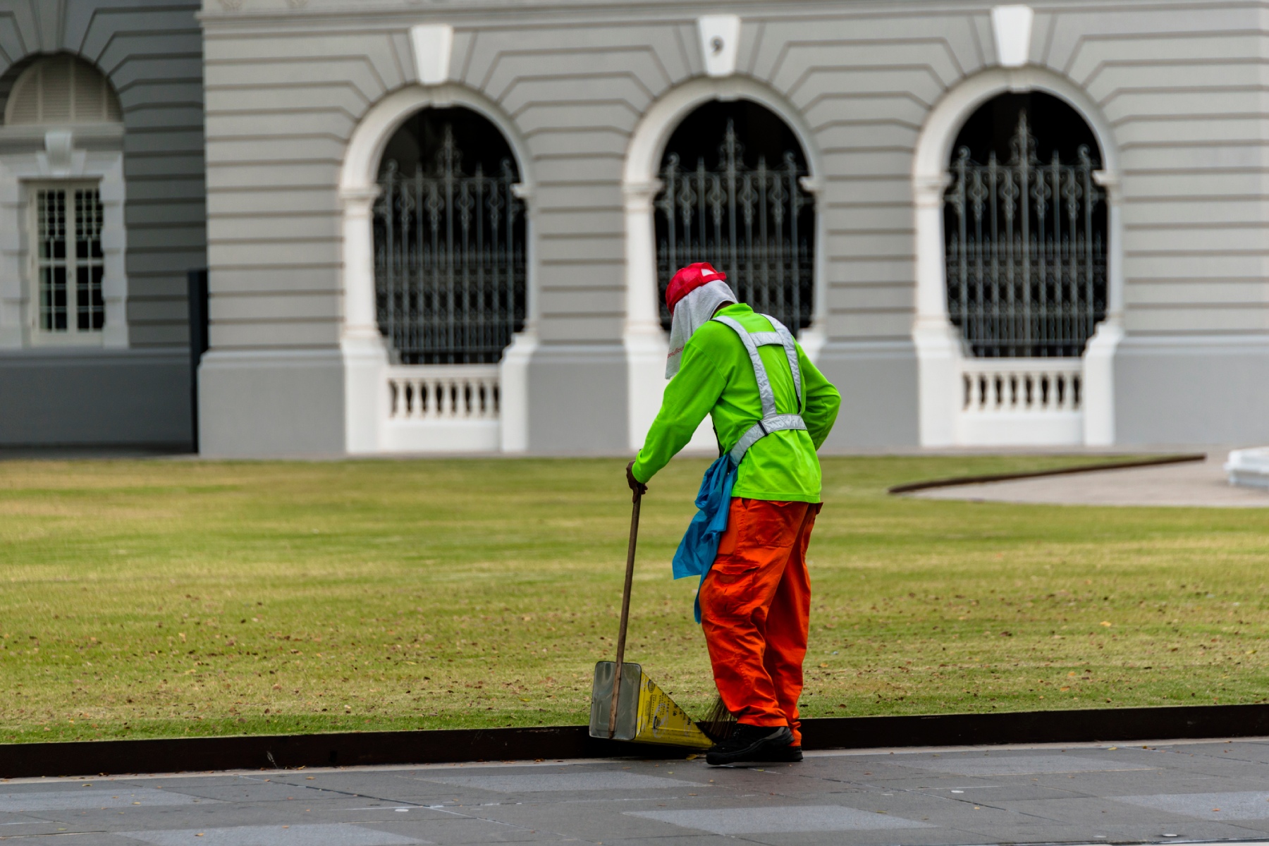 A street sweeper wearing a uniform and cleaning the pavement in front of a building in Singapore