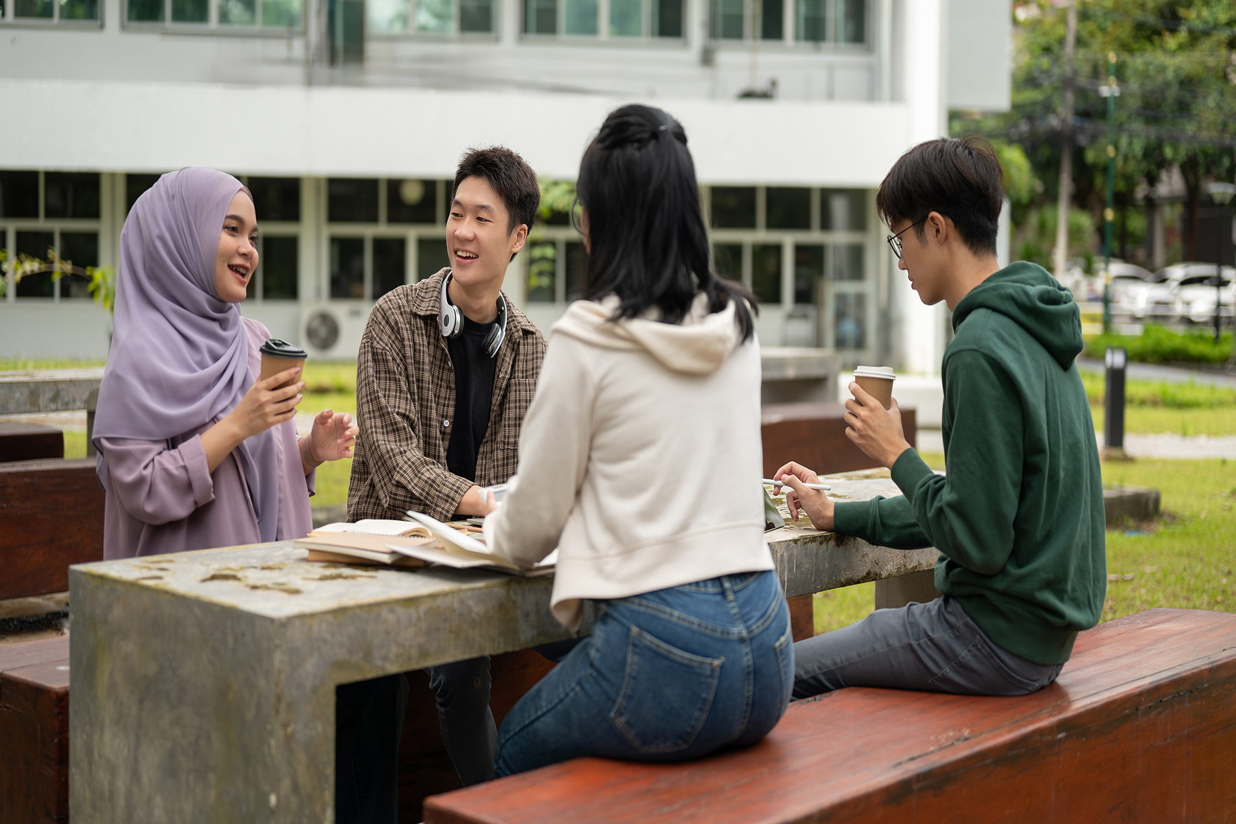 Four students sit on at a table outside and chat and laugh