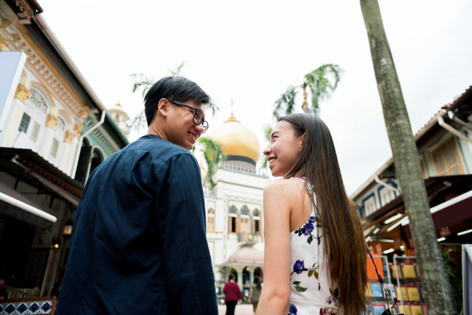 Couple standing near the Masjid Sultan in Singapore, looking at each other and smiling.