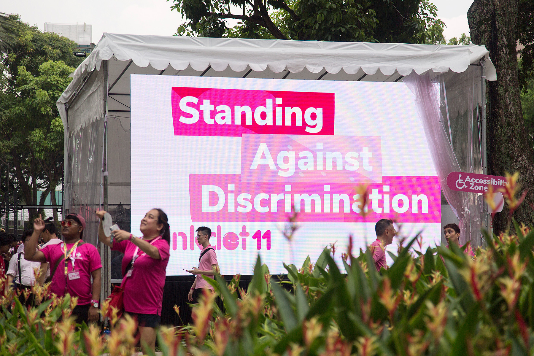 People walking past a pink and white banner that says 'Standing Against Discrimination' on it