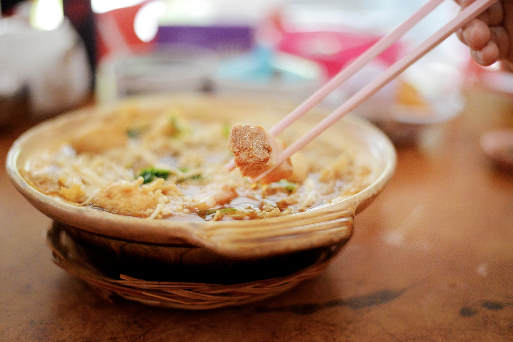 A close-up shot of a bowl of bak kut teh and a pair of chopsticks clasping a piece of pork. Bak kut teh (or 'meat bone tea') is a popular Chinese soup found in Singapore.