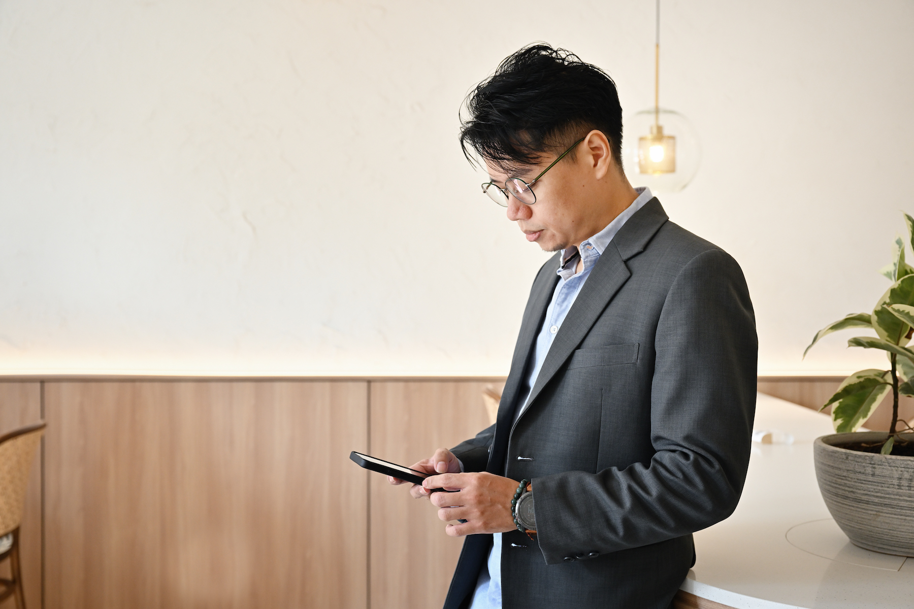 A man dressed in business attire looks down at his phone while he's waiting