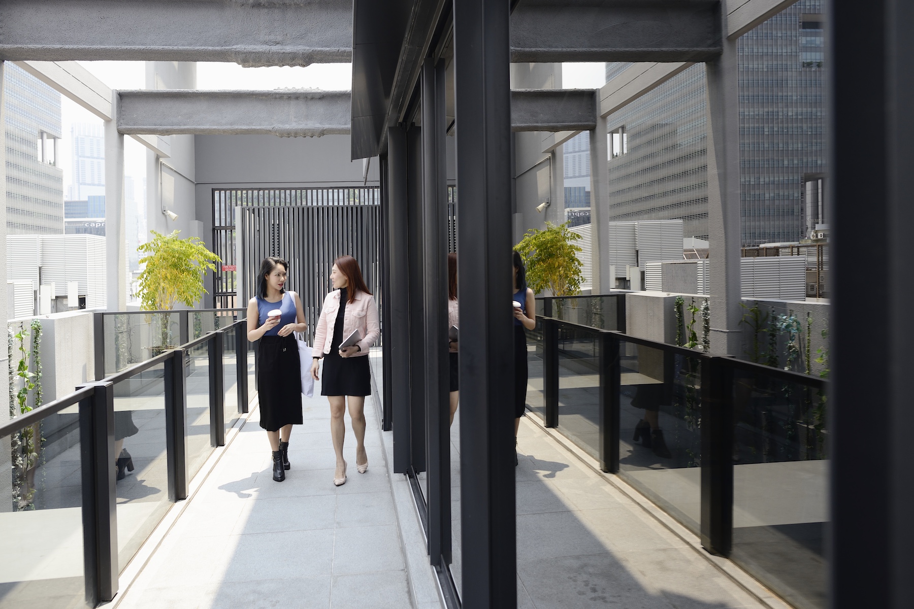 Two women dressed in business casual walk to a meeting together through their office's outdoor walkway
