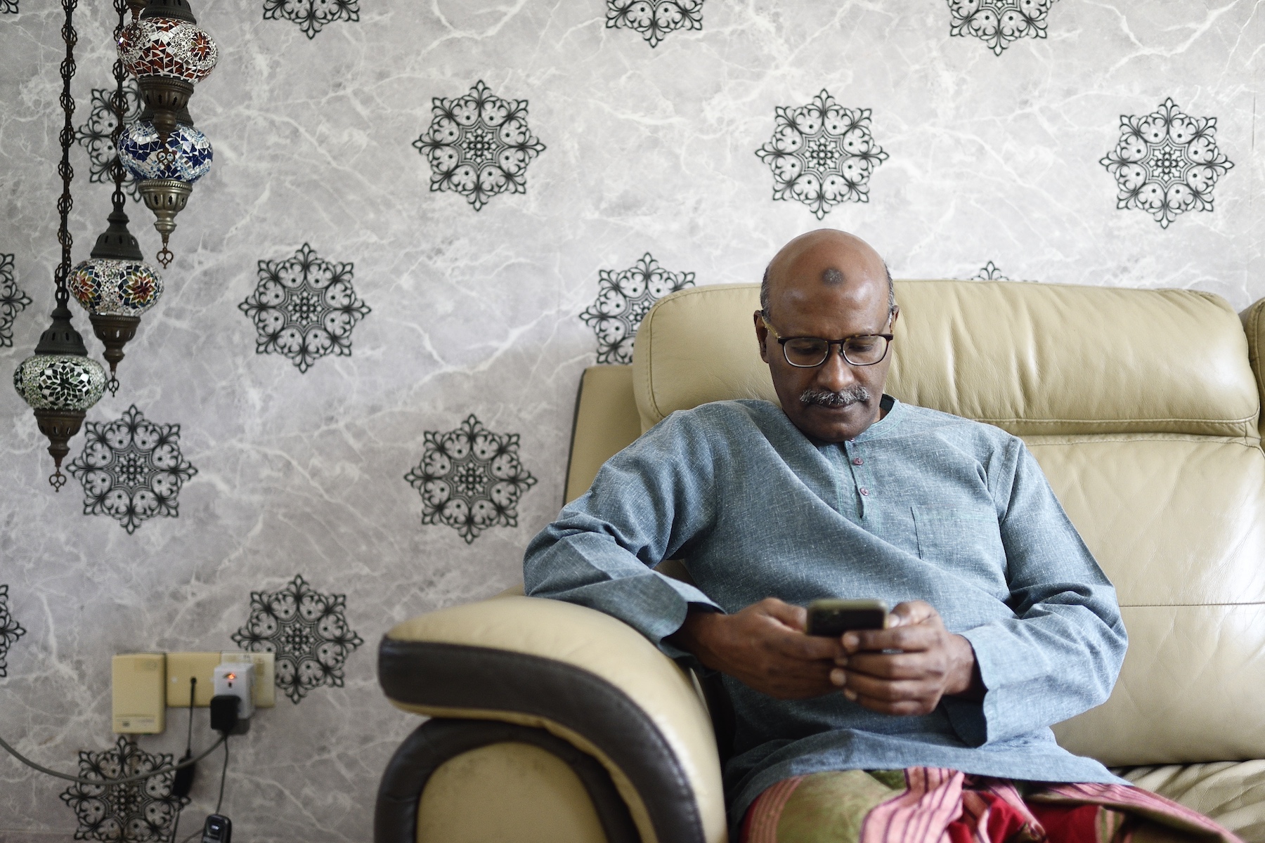 A man sits on the couch while typing something on his mobile phone
