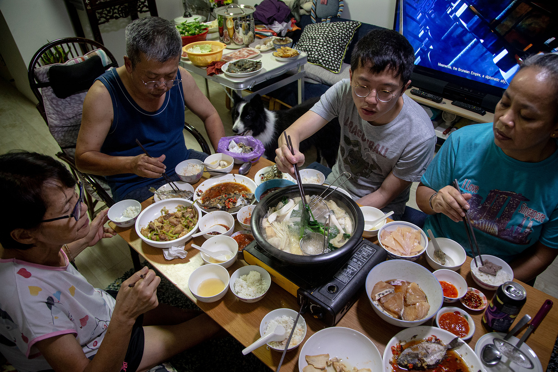 A family (three generations) having a steamboat dinner to celebrate Lunar New Year in Singapore, lots of small dishes on the table

