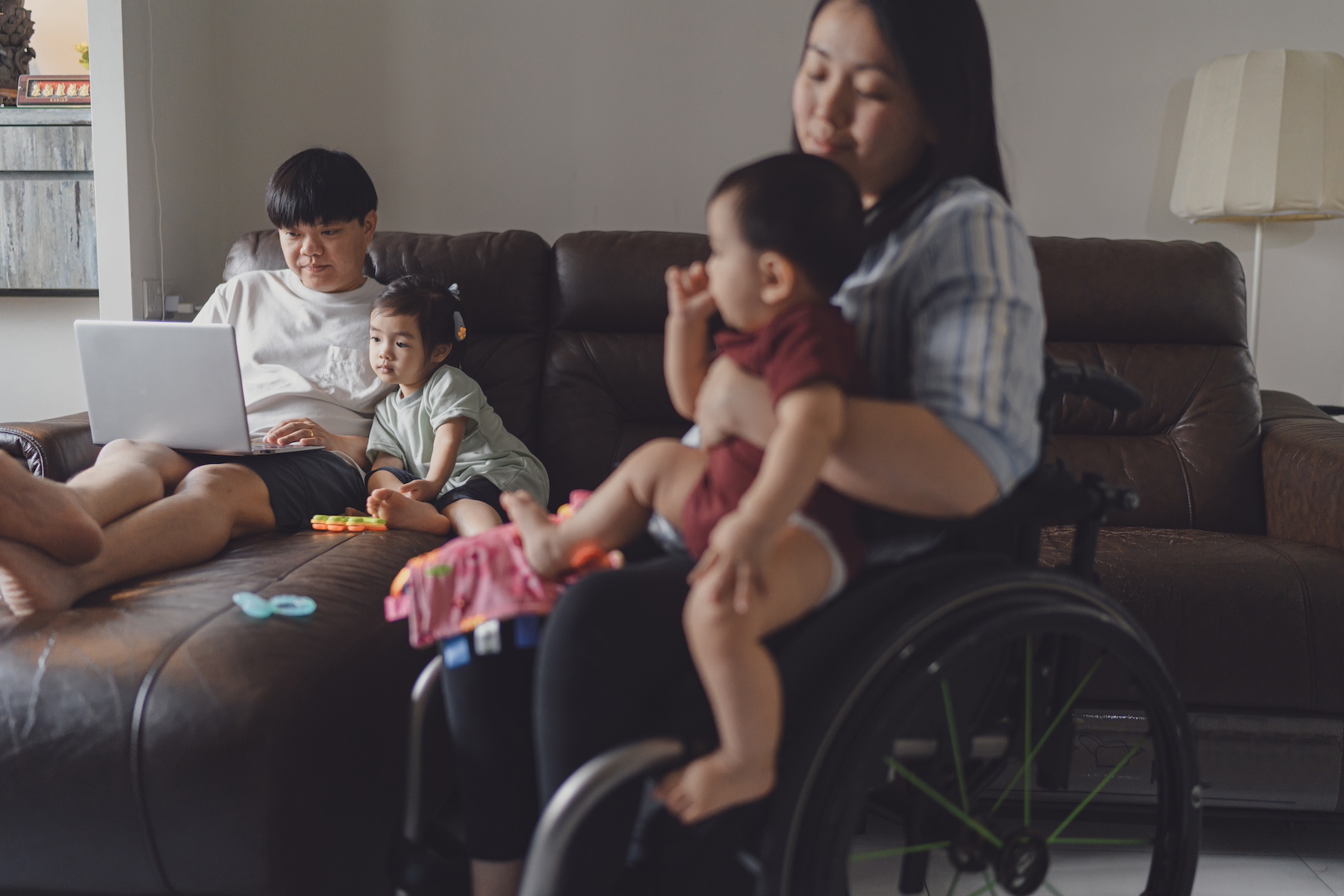 A family of four together in the living room, the mom is in seated in a wheelchair holding the baby