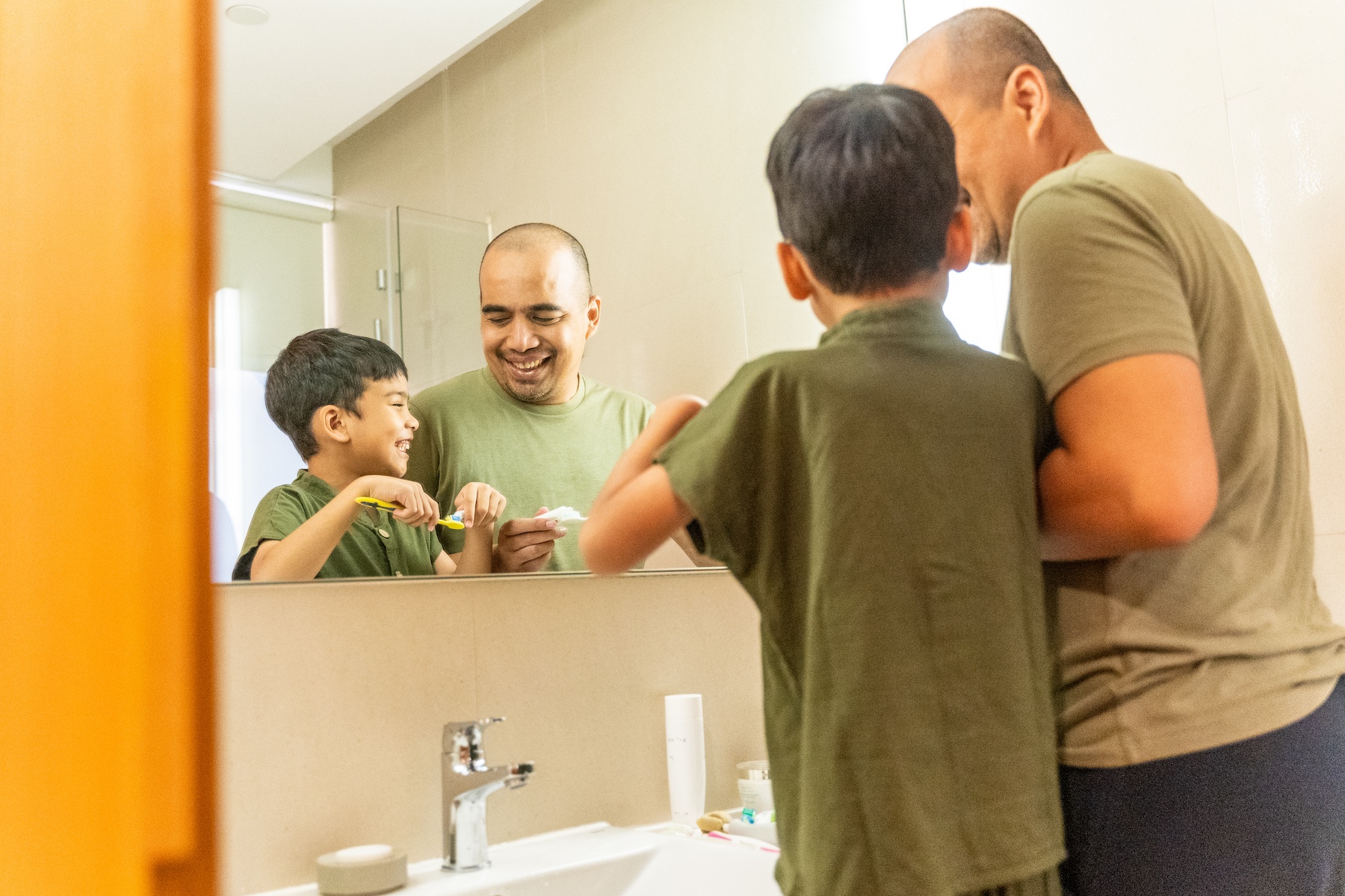 Father and son stand side-by-side brushing their teeth in the bathroom
