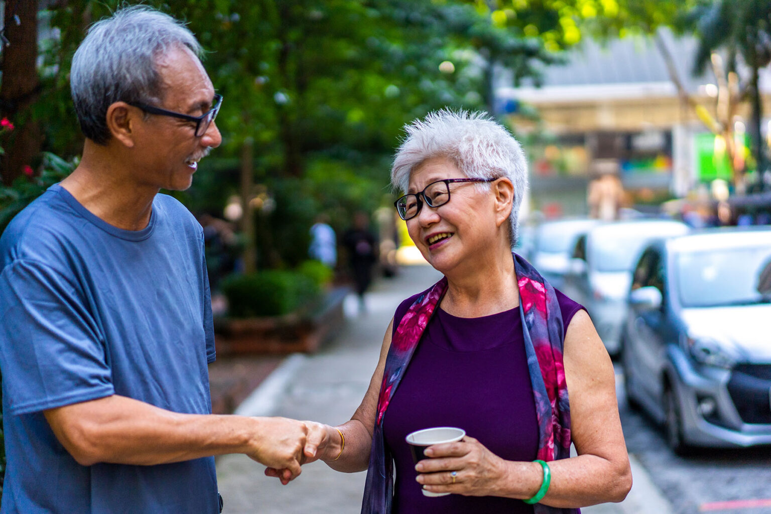 Two senior people shaking hands and talking while they are standing on the street in Singapore.